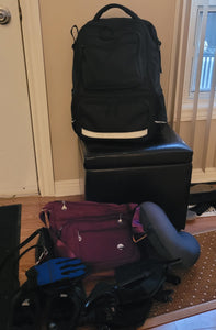 The purple bag is sitting in the middle of a pile of things ready for a trip.
