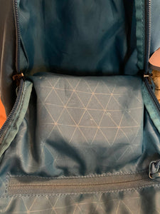 Looking into the open backpack, where a zipper pocket is visible and there is a light geometric design on the blue material.