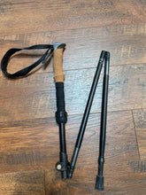 Load image into Gallery viewer, Black trekking pole with a cork grip and black wrist loop folded up in a z shape.
