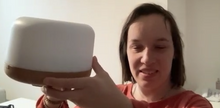 Load image into Gallery viewer, Hannah holds up a white, circular device with a brown base.
