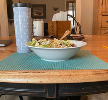 Load image into Gallery viewer, Teal shelf liner is cut into the shape of a placemat. The placemat is on a wooden table. On top of it are a bowl of salad and a water bottle.
