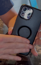 Load image into Gallery viewer, Black Otter + Pop Symmetry Phone Case being held by someone, showing the pop socket on the case.
