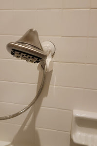 Silver shower head in the white shower head holder attached to a white tile while.