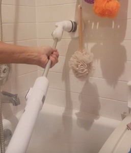 Action shot of Turbo Scrub Power Scrubber, with a hand holding the brush towards the front and the brush scrubbing the tile wall.