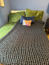 Load image into Gallery viewer, Dark gray chunky knit blanket spread out over one side of the bed that has green pillows.
