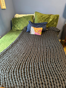 Dark gray chunky knit blanket spread out over one side of the bed that has green pillows.