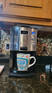 Coffee maker with a coffee mug that says "Woof" on it. The black caddy tray is barely noticeable underneath the machine unless you know it is there.