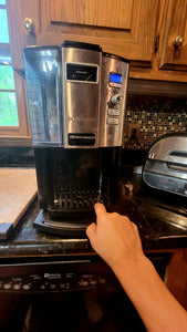 A coffee maker sitting on a black kitchen caddy (not really visible) is pulled to the front of the counter 
