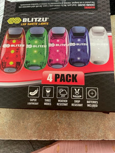 Packaging for Blitzu safety lights showing 5 lights of different colors (but they come in a pack of 4). The information on the pack says "Blitzu LED Safety Lights" - super lightweight, three modes, weather resistant, drop resistant, batteries included.
