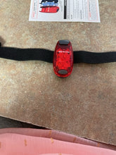 Load image into Gallery viewer, Safety light with velcro strap attached. The light is oval shaped and red, with a gray button at the bottom of it.
