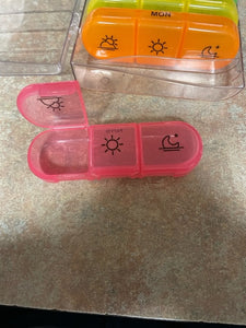 One compartment of the pink pill box is open and the other two are closed. The closed ones show a sun and a moon.