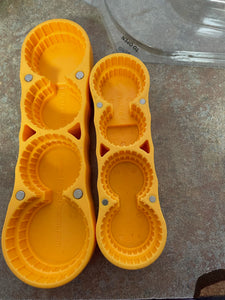 The bottoms of the yellow magic Opener regular and mini, showing four openings for different sized bottle lids in each one, with the mini having smaller sizes.  Small magnets are also visible, for hanging it on a fridge or other magnetic surface.