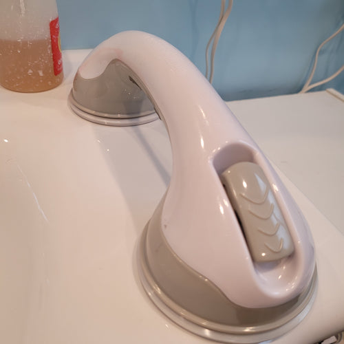 Lisa's portable grab bar attached to her sink, which is a smooth, non-porous, white, ceramic surface. The bar is white with gray fastening clips and gray around the suction cups.