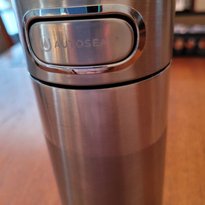 Close up of silver stainless steel Contigo Luxe Autoseal Mug and the button that is used to release the valve for drinking. The button says "autoseal" and is wider than it is tall.