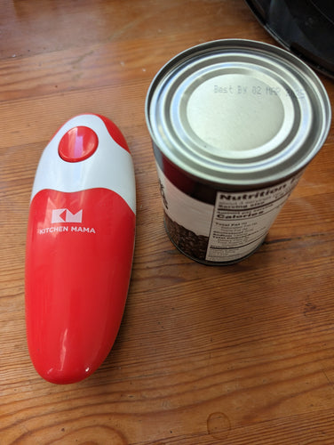 The Kitchen Mama 2.0 electric can opener in red and white sitting beside a can of beans on a table.