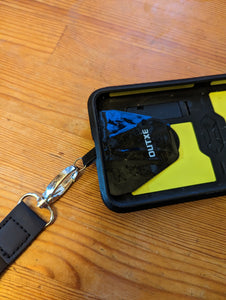 Close up of where the lanyard connects to the cell phone. A silver clasp on the lanyard connects to a black Outxe "pad" that is attached to the cell phone.