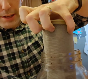 A person is removing the metal coffee filter from the mason jar.