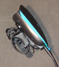 Load image into Gallery viewer, Side view of front light plugged into charging cable. Device is black with light blue accent and has a round loop strap with notches for attaching to device. 
