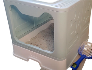 Post-cleaning view of the cat litter box. Light sea-foam green container with cat-shaped opening, white litter drawer/tray, and blue shovel tool beside the litter box. 