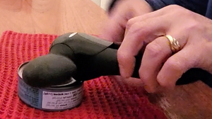 A person is holding the can opener against a tuna can, locking it onto the can prior to turning the knob.