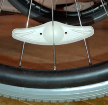 Load image into Gallery viewer, Spoke light is attached to spoke on a wheelchair wheel. It is not lit up and looks like small plastic wings, going across 3 spokes.
