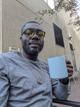 Load image into Gallery viewer, Tony, a black man with a trimmed beard, glasses, a gray shirt and a silver chain, is holding the blue MiiR mug.
