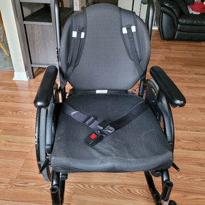 View of the straps holding the bag on the wheelchair, from the front of the wheelchair. The straps are on the back of the chair like a backpack.