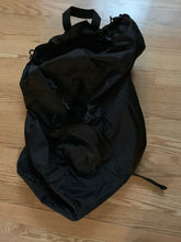 Load image into Gallery viewer, Large black bag with visible handle on a wood floor
