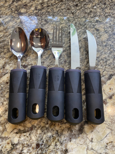 Five stainless steel utensils with thick, black grips around the entire handle and holes through the end (for hanging). From left to right, they are a regular spoon, a soup spoon, a fork, a regular knife and a slightly shorter, more curved knife.