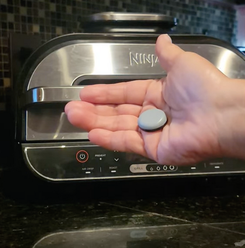 A hand with a gray appliance slider in front of a Ninja Air Fryer Grill 