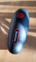 Load image into Gallery viewer, The top of a black, long oval can opener on a wooden table. The Bestday logo is in white text with a red ring around it. There is one large red &quot;on/off&quot; button toward the front.
