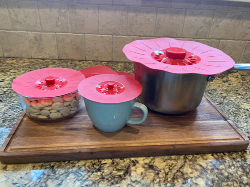 Red silicone lids of different sizes visible on a large pot, a blue mug, and a small dish with oyster crackers inside.