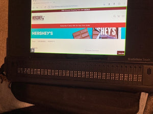 The tablet screen shows the Hershey's website. Beneath the screen is are 32 braille cells that go across the length of the device.