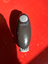 Load image into Gallery viewer, A top view of the jar opener device, which is black and oval shaped with a large gray button on top. It is sitting on a bright red surface.
