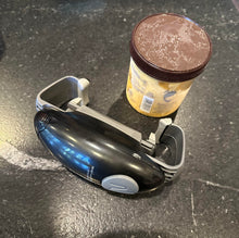 Load image into Gallery viewer, A black device with a gray button and gray pieces on its sides is on its side on a counter sitting beside a small tub of ice cream.
