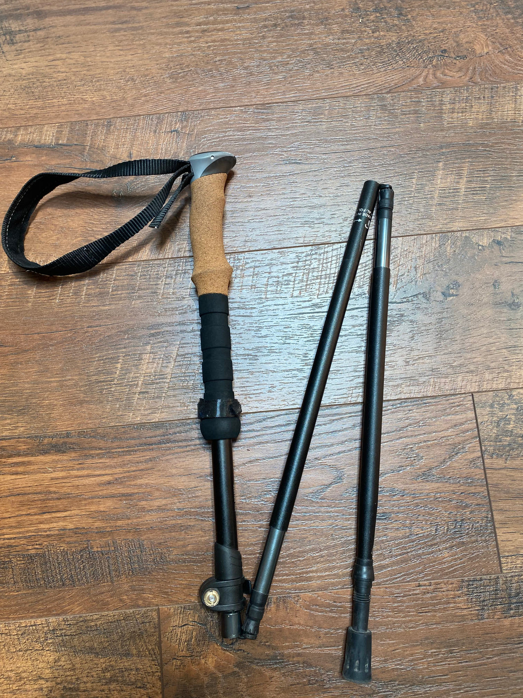 Black trekking pole with a cork grip and black wrist loop folded up in a z shape.