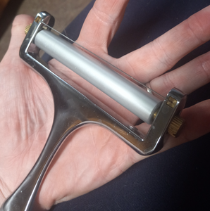 Metal device with a roller at the top with a thin wire above it and a metal handle. There are knobs on either side of the roller.