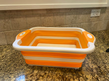 Load image into Gallery viewer, The cutting board is pulled up into the basket function. It is orange and white and sitting on a marble countertop.
