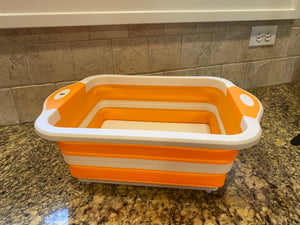 The cutting board is pulled up into the basket function. It is orange and white and sitting on a marble countertop.