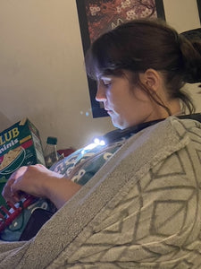 Side view of Jessica wearing the neck lamp, which is on, while she is doing a craft. The lights on the device are pointed down towards her hands.