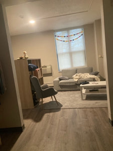 gray couch, the white coffee table in front of it, the gray plush armchair with storage shelves near the coffee table, and a window behind the couch with multicolored hearts above it