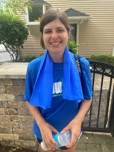 Ellie, a white woman with brown hair pulled back, is smiling and wearing the blue cooling towel around her neck.