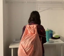 Load image into Gallery viewer, A person with long brown hair is wearing a large neon orange laundry backpack on her back. The drawstring is pulled around to the front.

