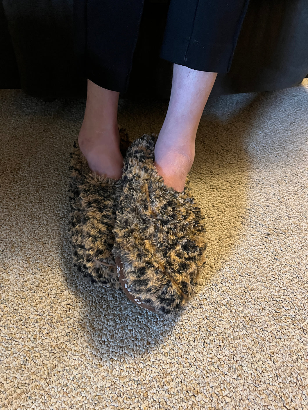 Shaggy leopard slippers on a person's feet.