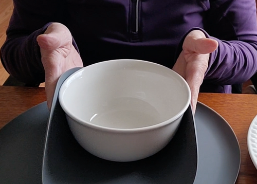 A gray microwave mat is pulled up on the sides to hold a ceramic bowl. The mat is protecting the person's hands from touching the bowl.