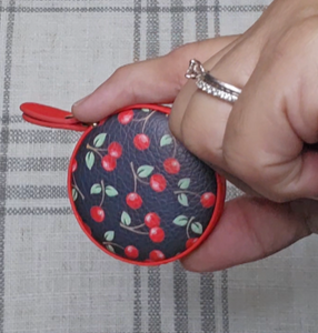 Small round measuring tape in black faux leather case with red trim, red cherries, and a red pull on the measuring tape