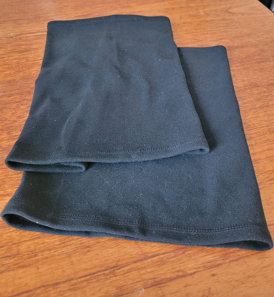 Two black fleece neck warmers are laid out on a wooden table.