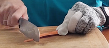 Load image into Gallery viewer, A person is wearing a gray and white glove on the hand holding a carrot steady on the chopping board and using a large knife to chop with the other hand.
