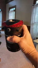 Load image into Gallery viewer, A person holding the closed camping lantern. The top of it is more visible, including the red parts for emergency flashing and the top for the flashlight.
