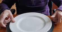 Load image into Gallery viewer, A dinner plate sits on top of a gray microwave mat on a wood table.
